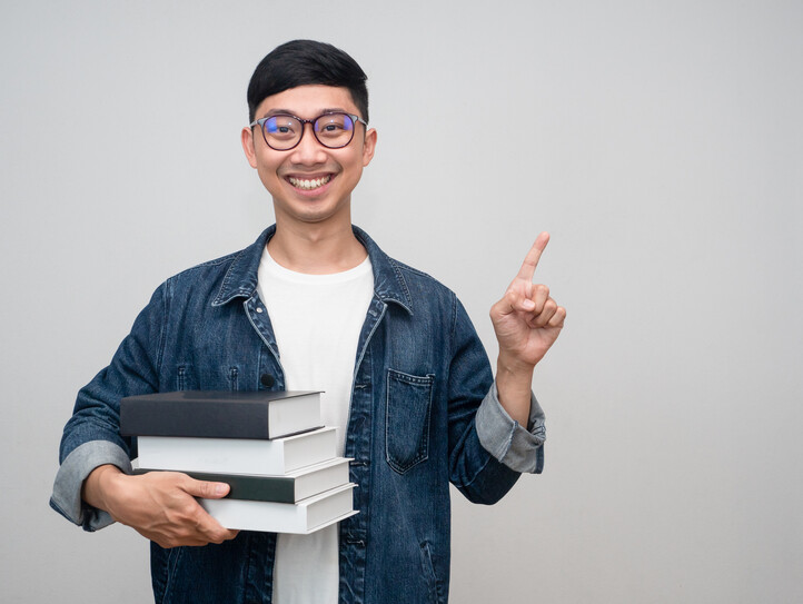 Portrait young man wear glasses jeans shirt holding the books happy smile point finger isolated